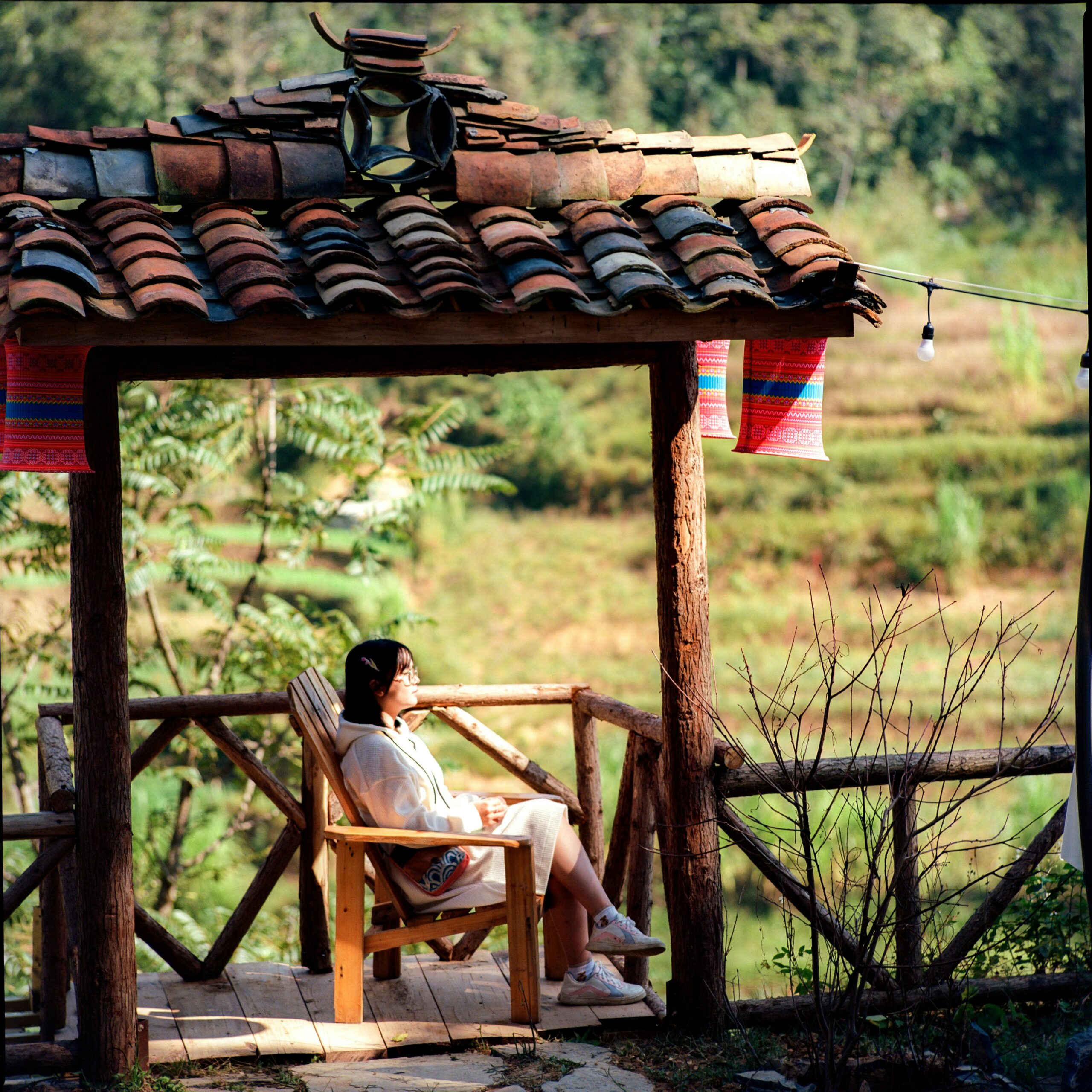 Woman relaxing in a gazebo chair with countryside views, enjoying a sunny day outdoors.